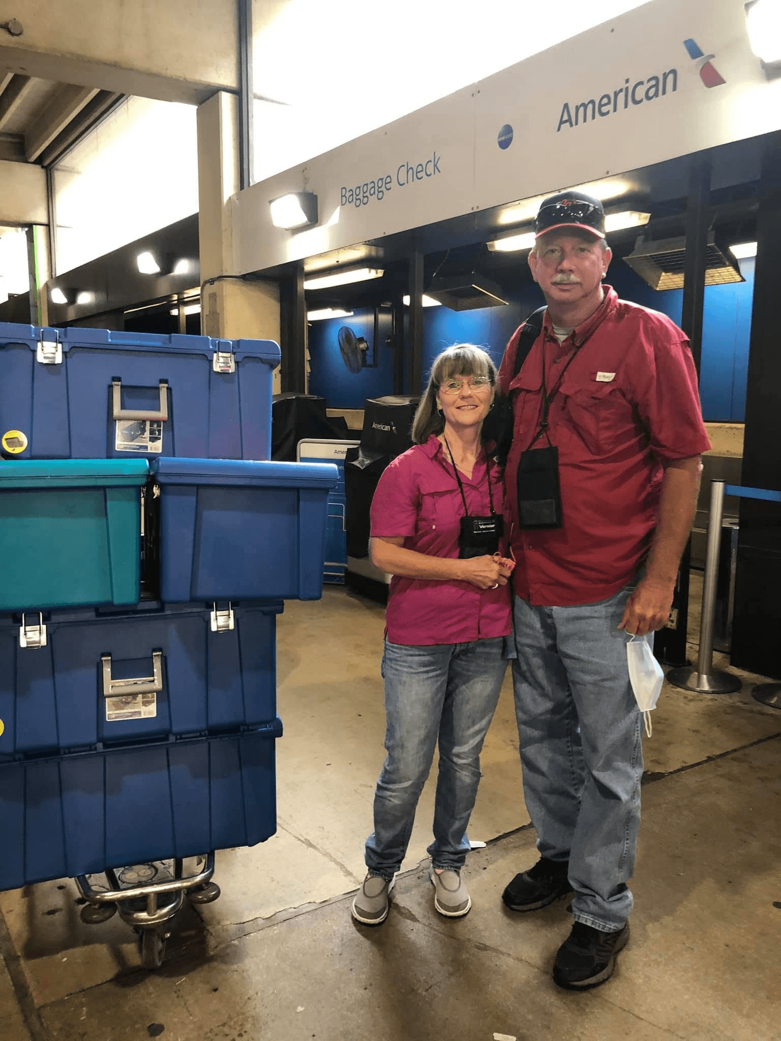 Don and Patti Nichols standing together beside stacked travel trunks at an airport